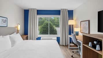 A hotel room with a large bed, a desk with a chair, a television, and a window with curtains.