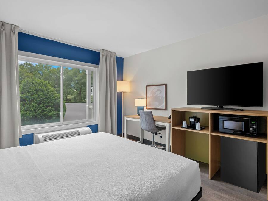 Habitació d'hotel amb llit, escriptori, cadira, televisió, microones i una finestra amb cortines.