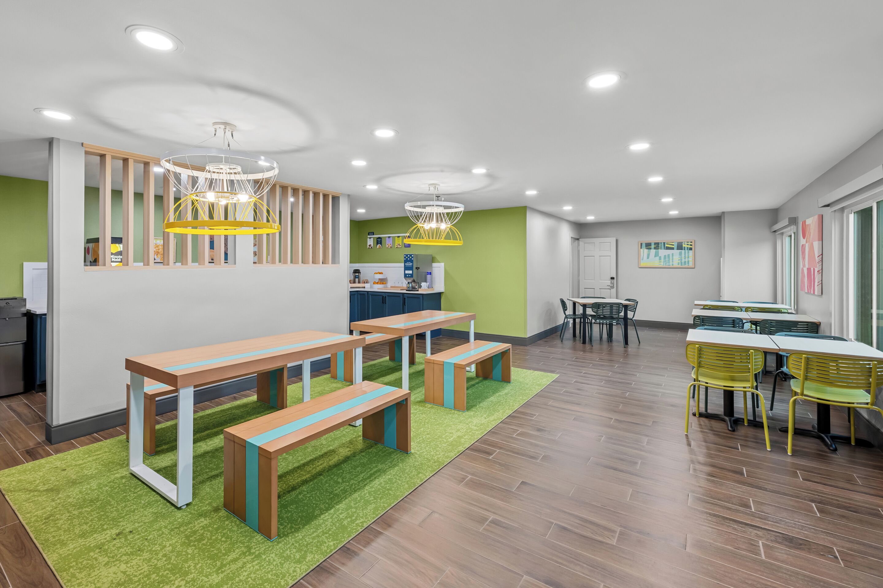 A spacious room with wooden benches, a green carpet, and a kitchen area in the background.