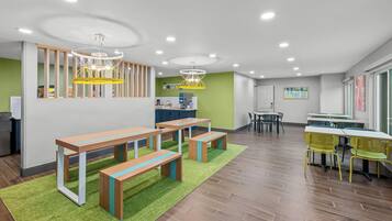 A spacious room with wooden benches, a green carpet, and a kitchen area in the background.