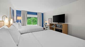 A hotel room with two beds, a television, a desk with a chair, a microwave, and a window with curtains.