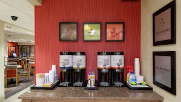 A coffee station with multiple coffee dispensers labeled 'Dark Roast,' 'Light Roast,' 'Decaf,' and 'Hot Water.' There are stacks of disposable cups and a tray with condiments and napkins.