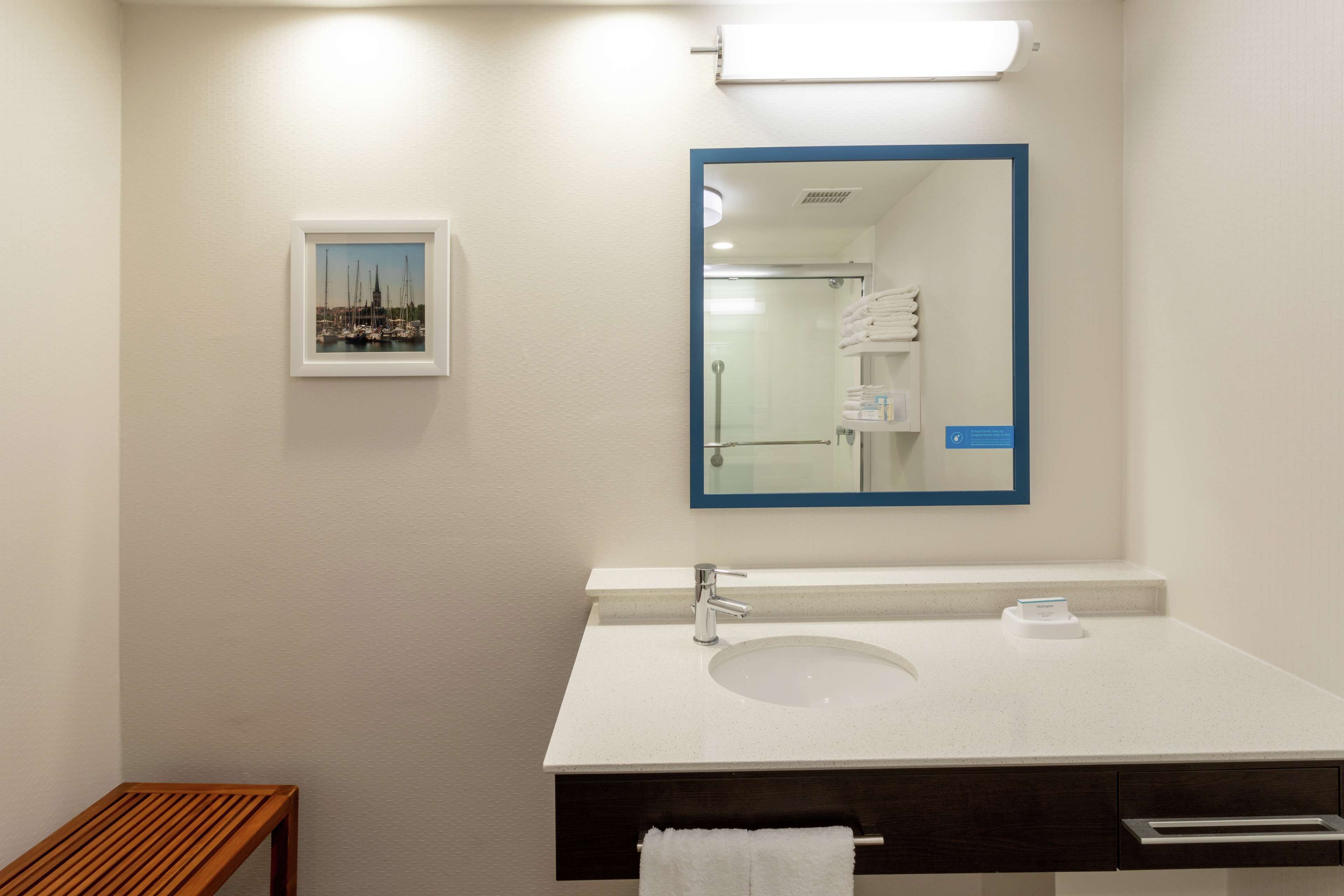 A modern bathroom with a white sink, a mirror with a blue frame, and a framed picture on the wall.