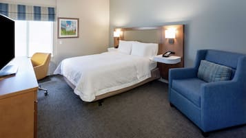 A hotel room with a bed, a desk, a chair, and a nightstand with a lamp.