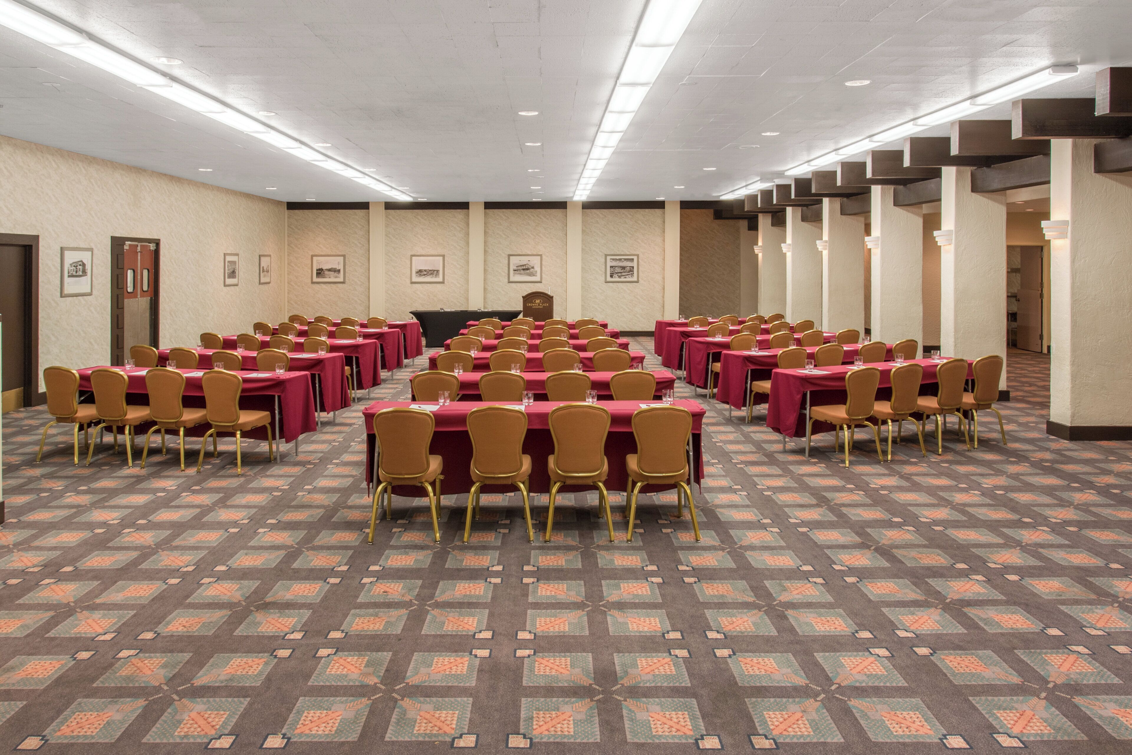 A conference room with rows of tables and chairs, a podium, and framed pictures on the walls.
