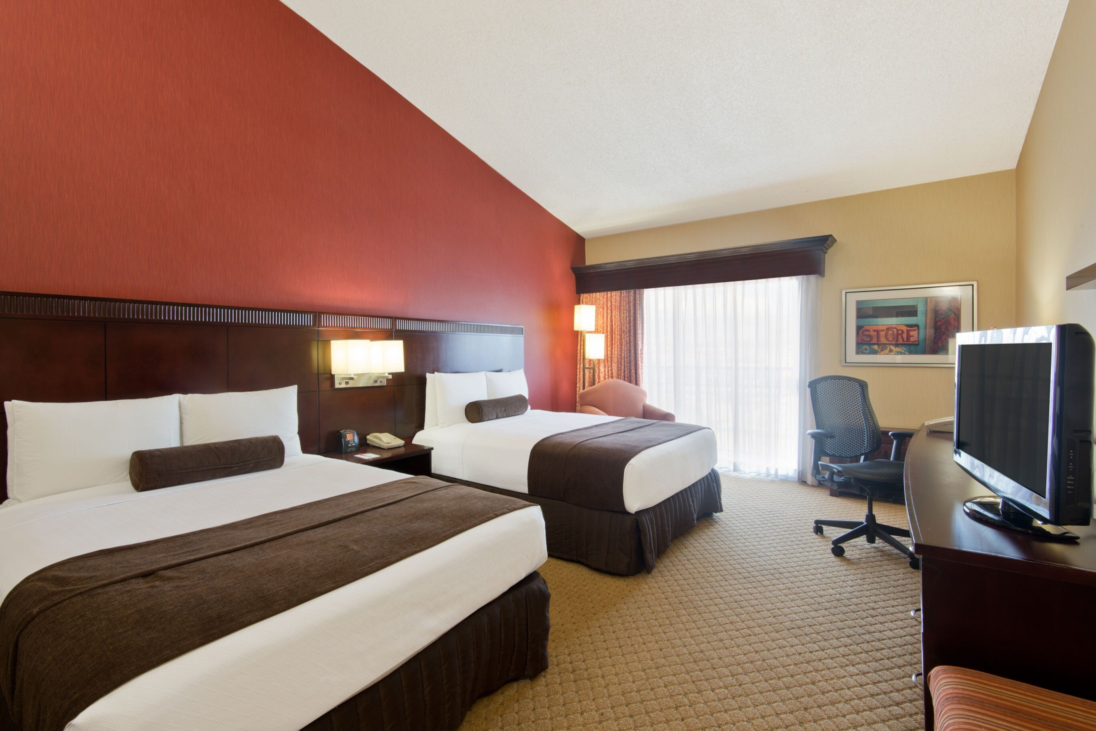 A hotel room with two beds, a desk, a chair, a television, and a window with curtains.