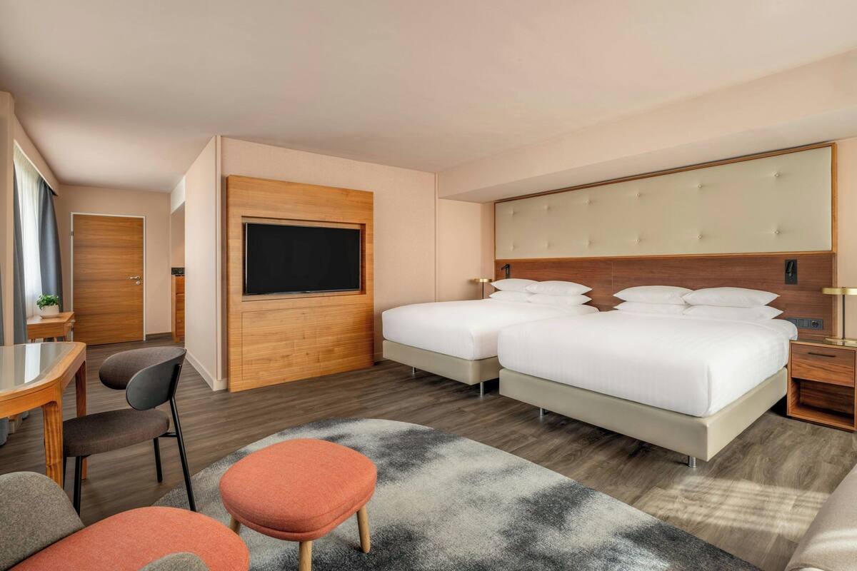 Hotellihuone, jossa on kaksi sänkyä, työpöytä, televisio ja pieni oleskelualue.