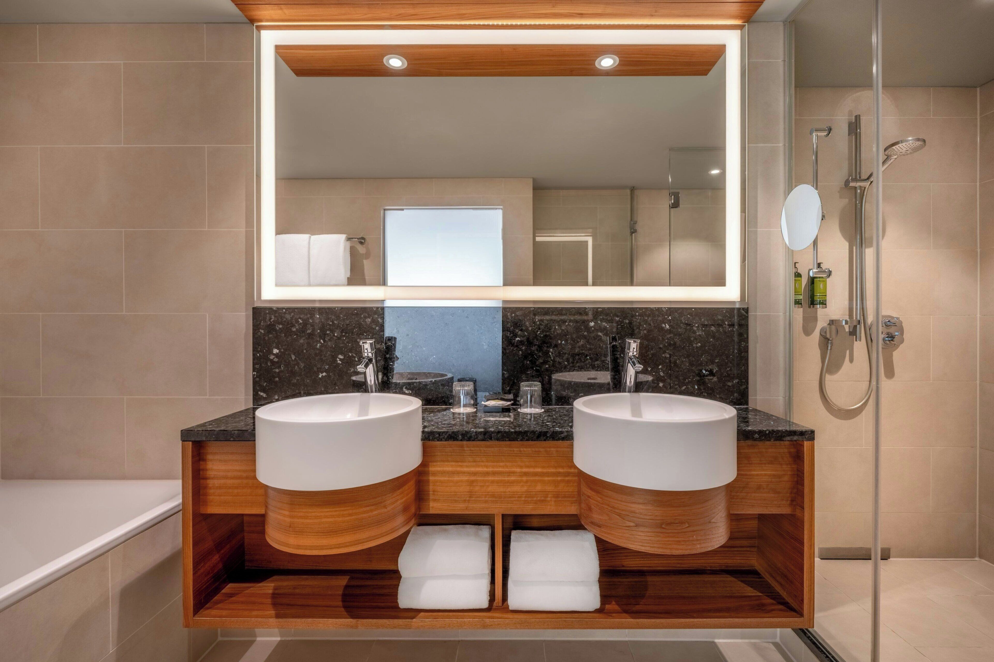 A modern bathroom with two sinks, a large mirror, and a shower.