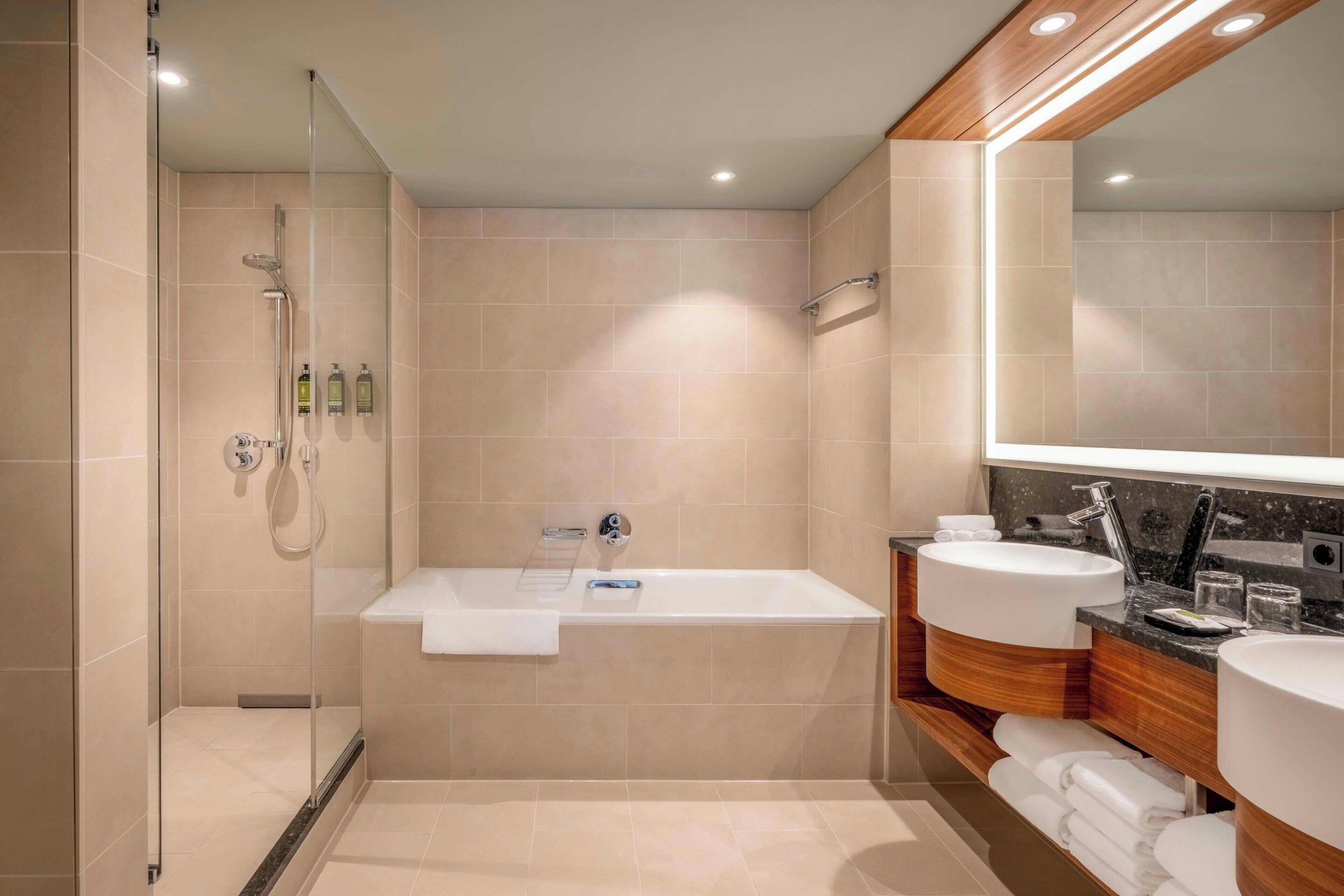 Ein modernes Badezimmer mit einer Glaskabine zur Dusche, einer freistehenden Badewanne und zwei Waschbecken mit Waschtisch.