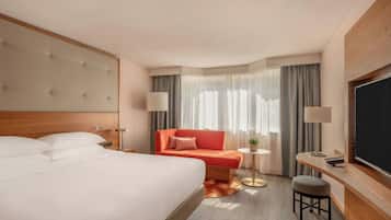 Habitación de hotel con una cama grande, un sofá, una mesita, un televisor y una ventana con cortinas.