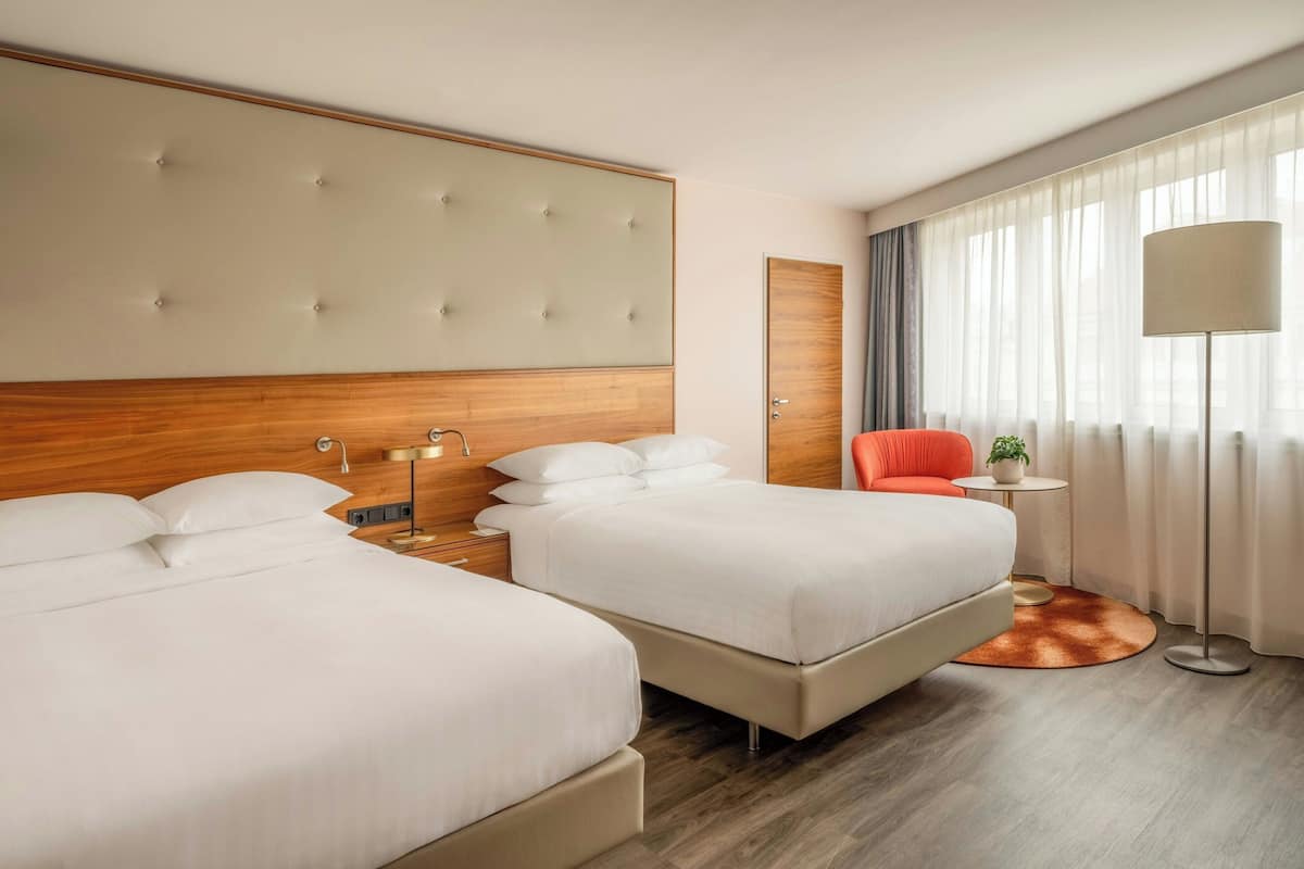 Hotellihuone, jossa on kaksi sänkyä, puinen pääty, pieni pöytä lampun kanssa ja suuri ikkuna, josta on näkymä ulos.