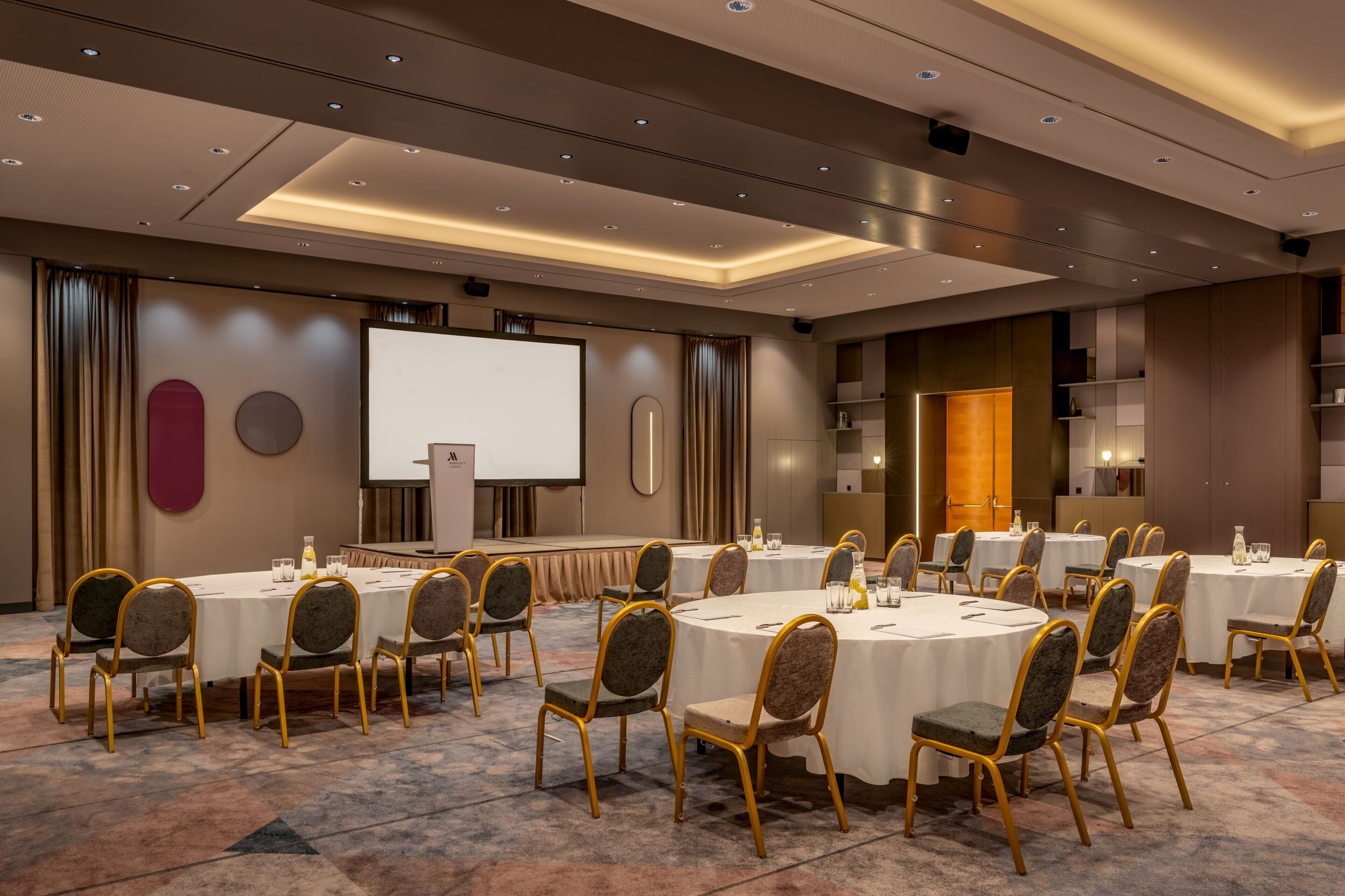A conference room with round tables and chairs, a projector screen, and a presentation podium.