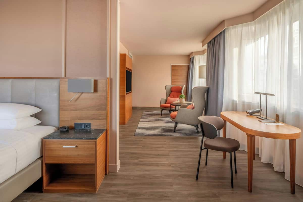 Hotellihuone, jossa on sänky, työpöytä, tuoli, televisio ja ikkuna, jossa on verhot.