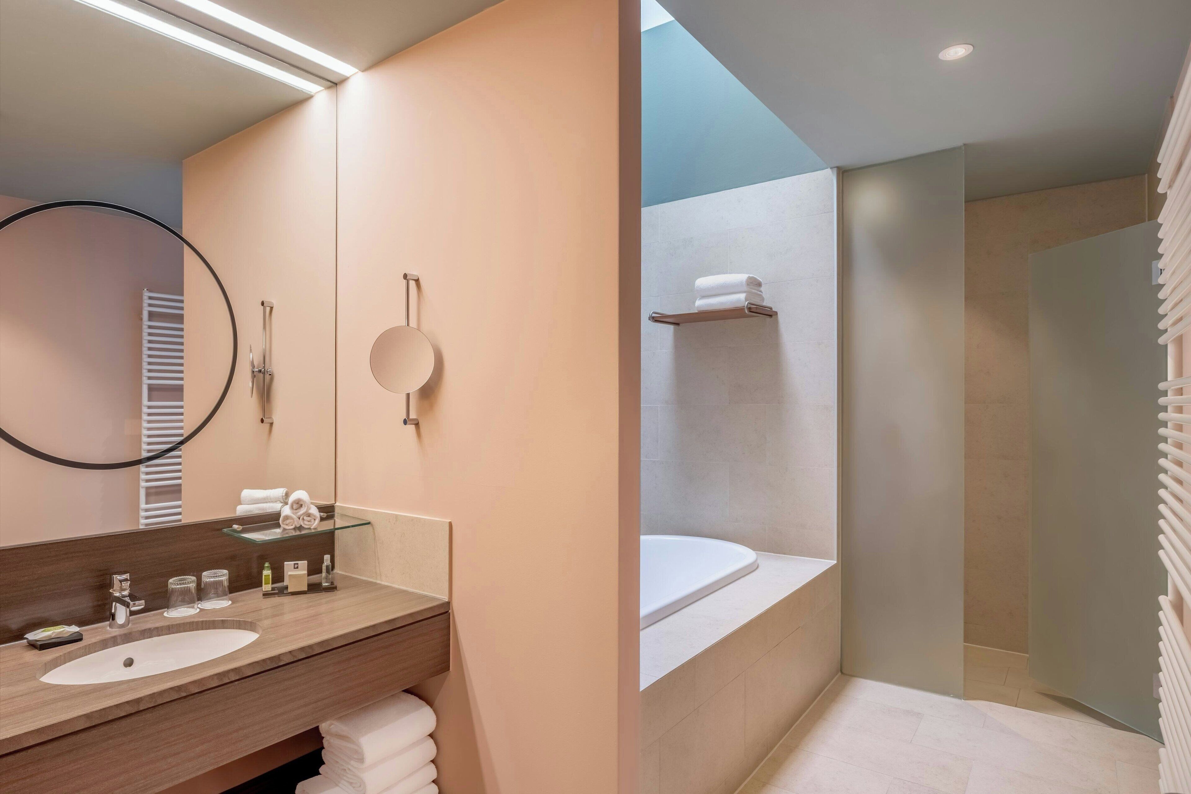A modern bathroom with a large mirror, a sink, and a bathtub.