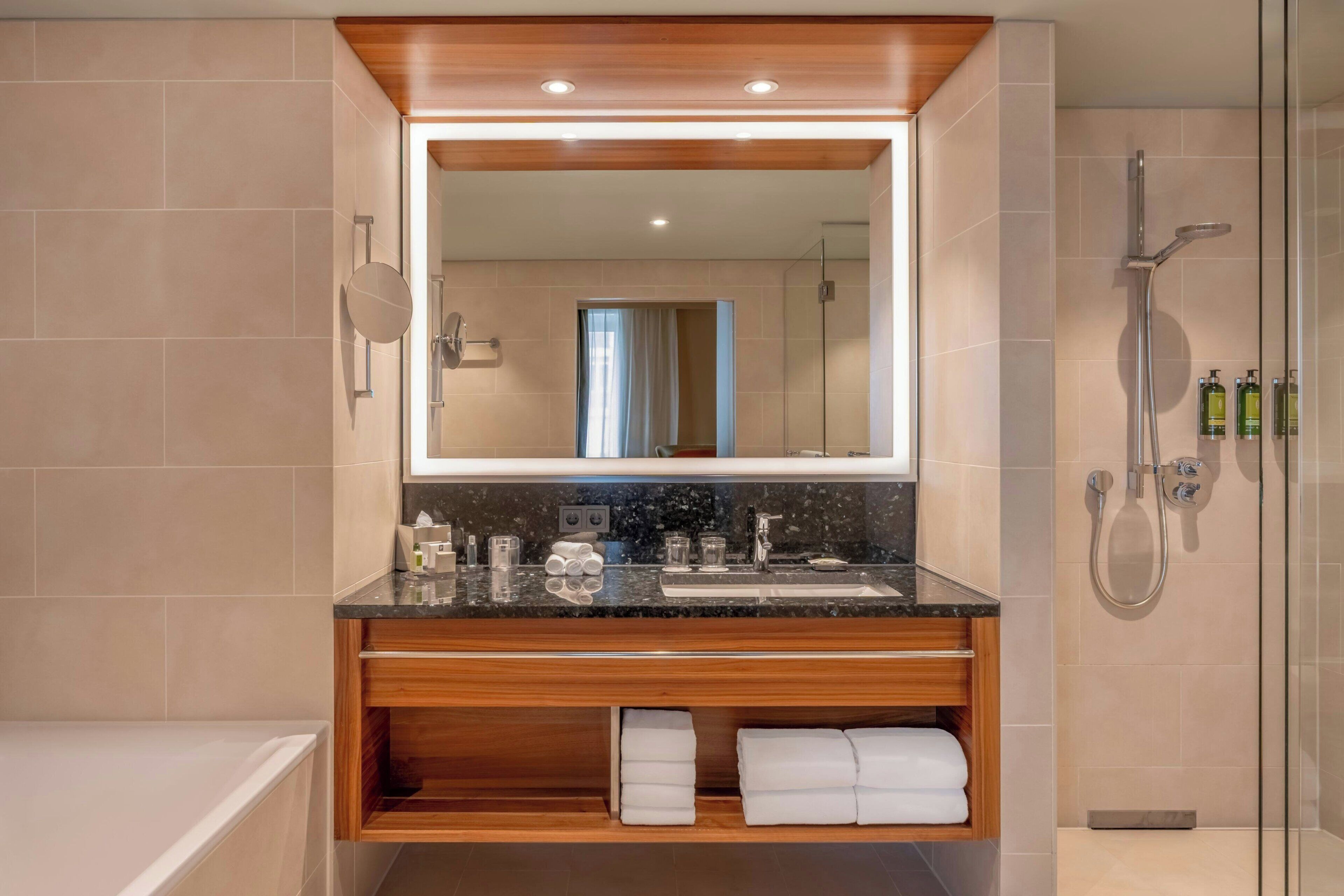 A modern bathroom with a large mirror, a sink, a shower, and a bathtub.