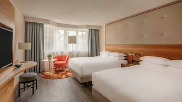 A hotel room with two beds, a desk with a chair, a small table with a plant, and a TV.