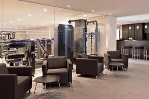 A modern fitness center with exercise equipment, seating areas, and a bar.