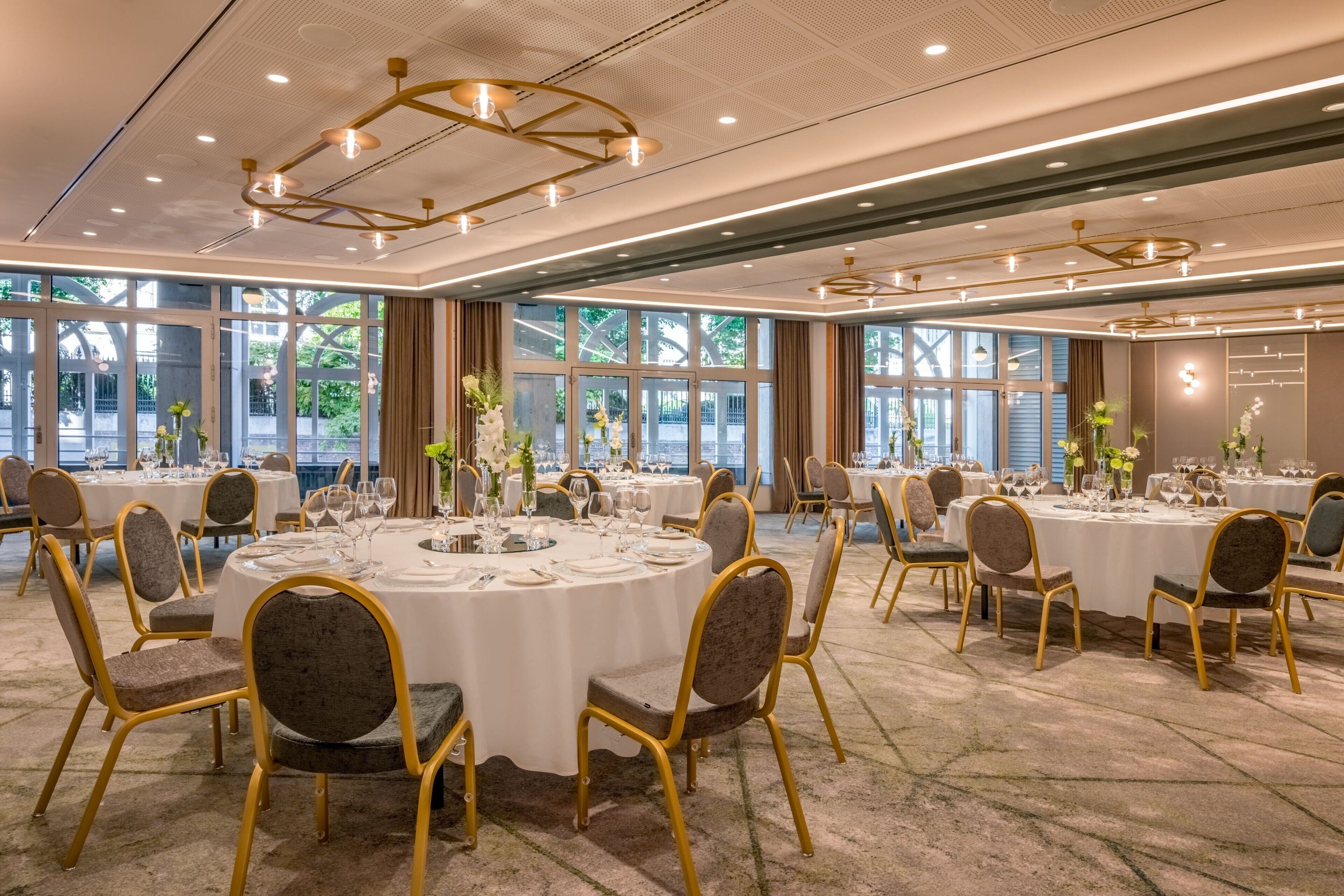 Uma sala de banquetes com mesas redondas, cadeiras e lustres.