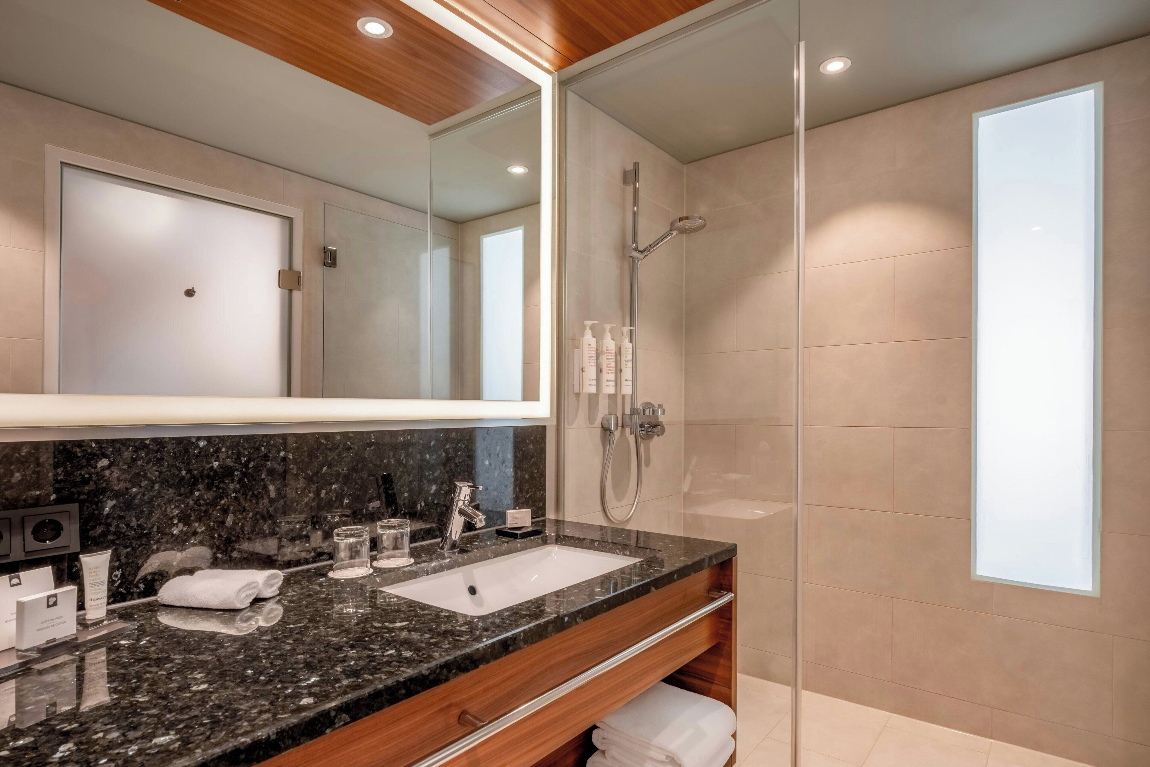 A modern bathroom with a granite countertop, a glass-enclosed shower, and a large mirror.