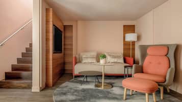 Uma sala de estar moderna com sofá, poltrona e mesa de centro, uma TV fixada na parede e uma escada que dá para outro andar.