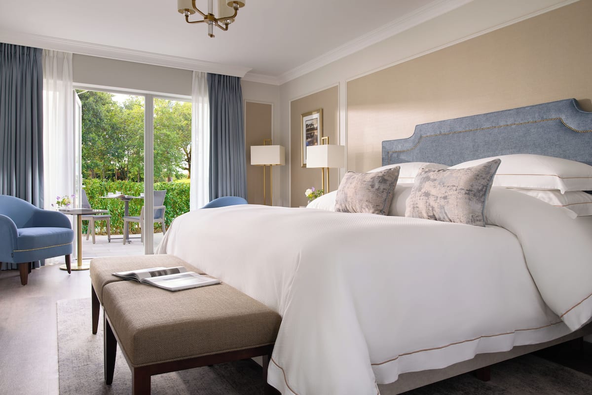 Ein geräumiges Schlafzimmer mit einem großen Bett, einem kleinen Tisch und einem Sessel. Ein Balkon bietet Blick auf grüne Natur.