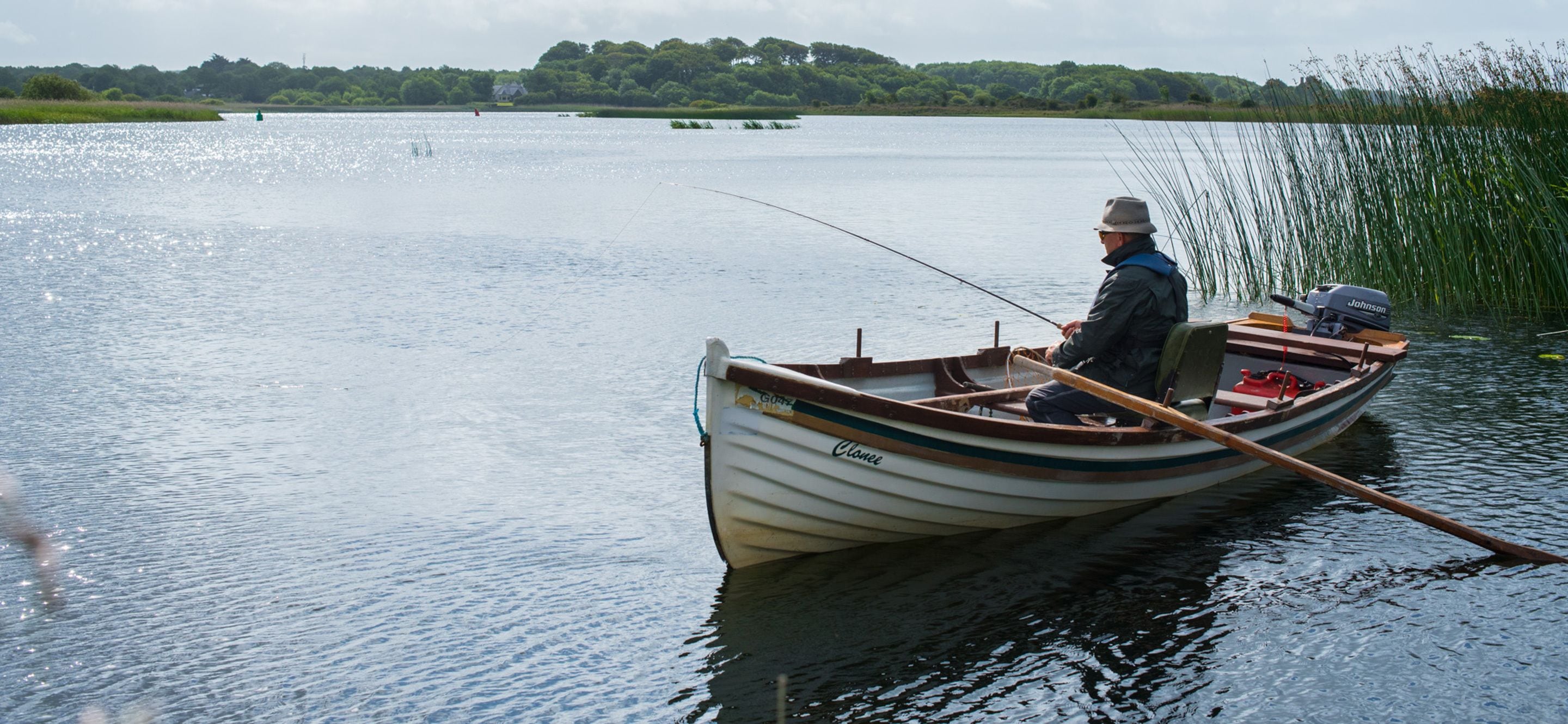 A man fishing from a small rowboat on a calm lake.