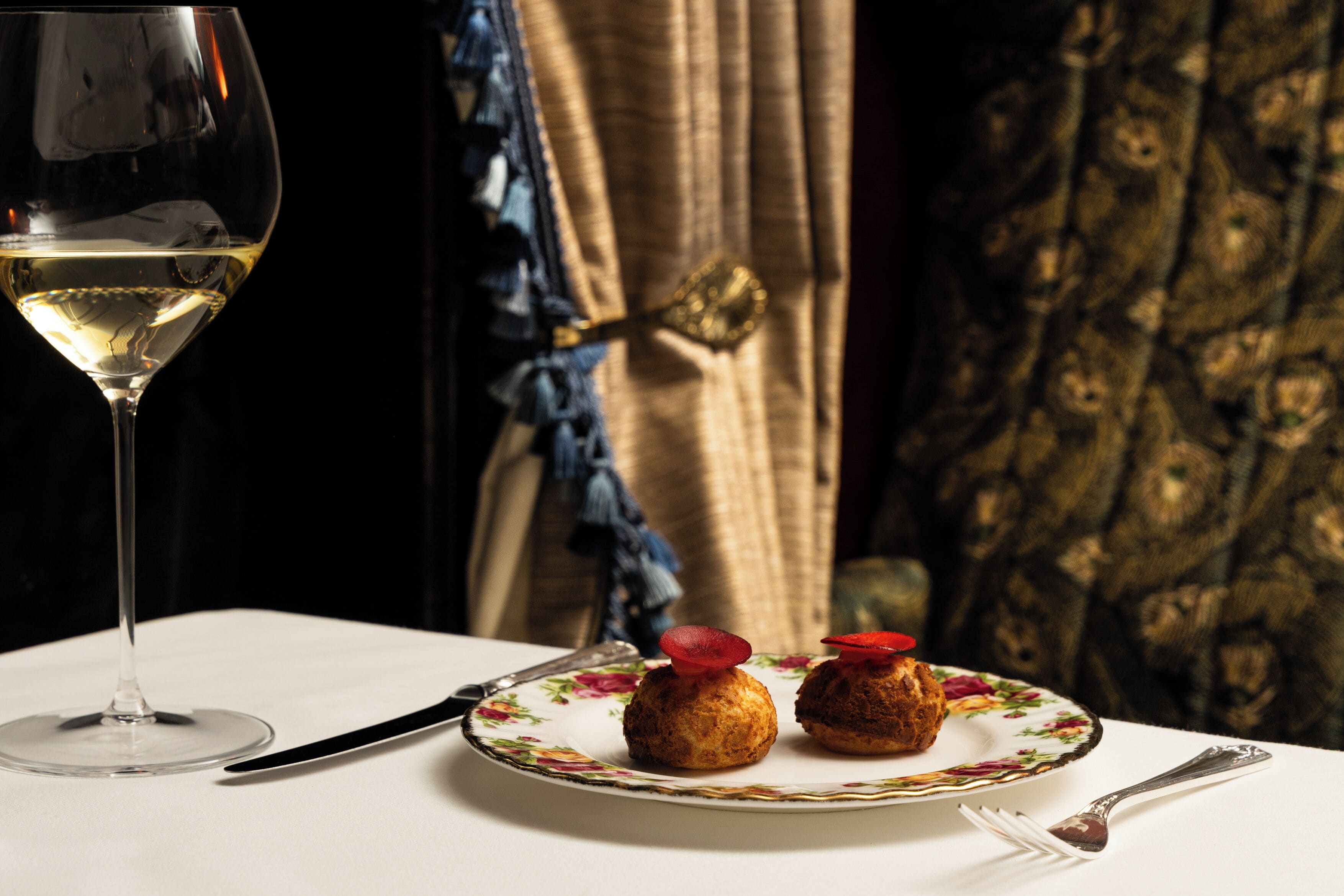 A table with a wine glass, a plate with two pastries, a knife, and a fork.