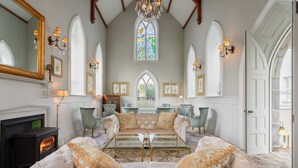 A spacious living room with a fireplace, comfortable seating, and a large window with stained glass. - Glenlo Abbey Hotel (Galway)