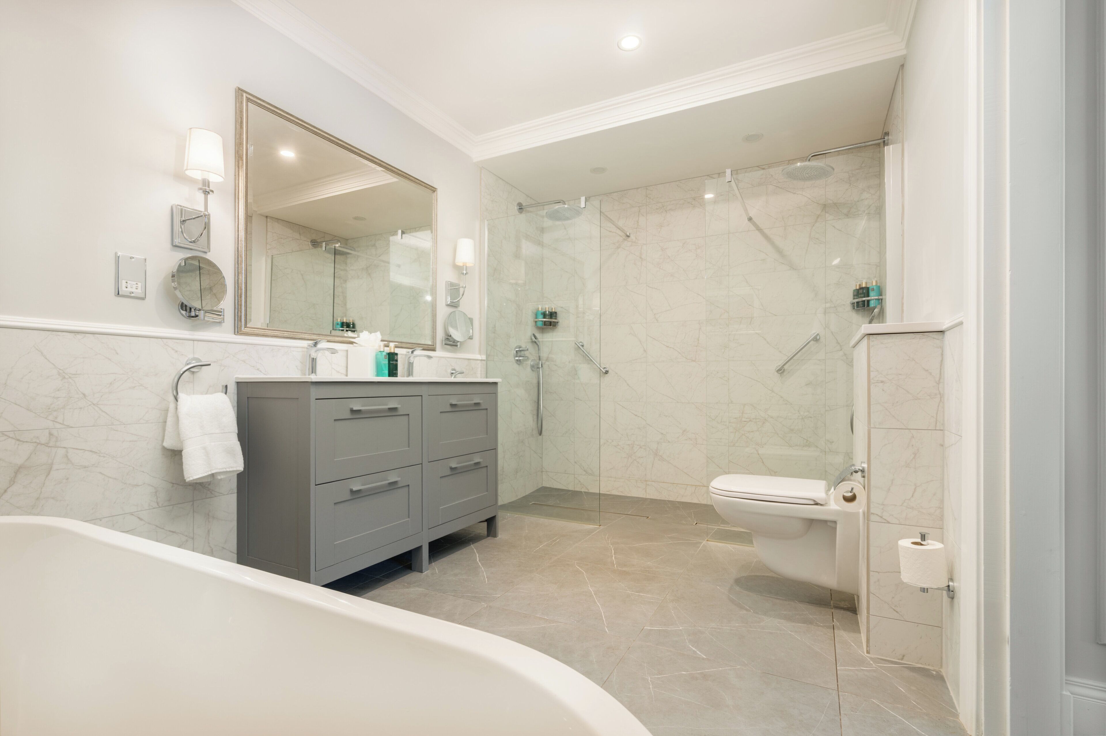 Un baño moderno con bañera, tocador gris y zona de ducha con mampara de cristal.