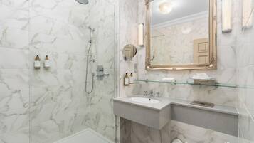 Un baño con suelo de mármol, mampara de vidrio, lavabo con espejo y artículos de aseo en la encimera.