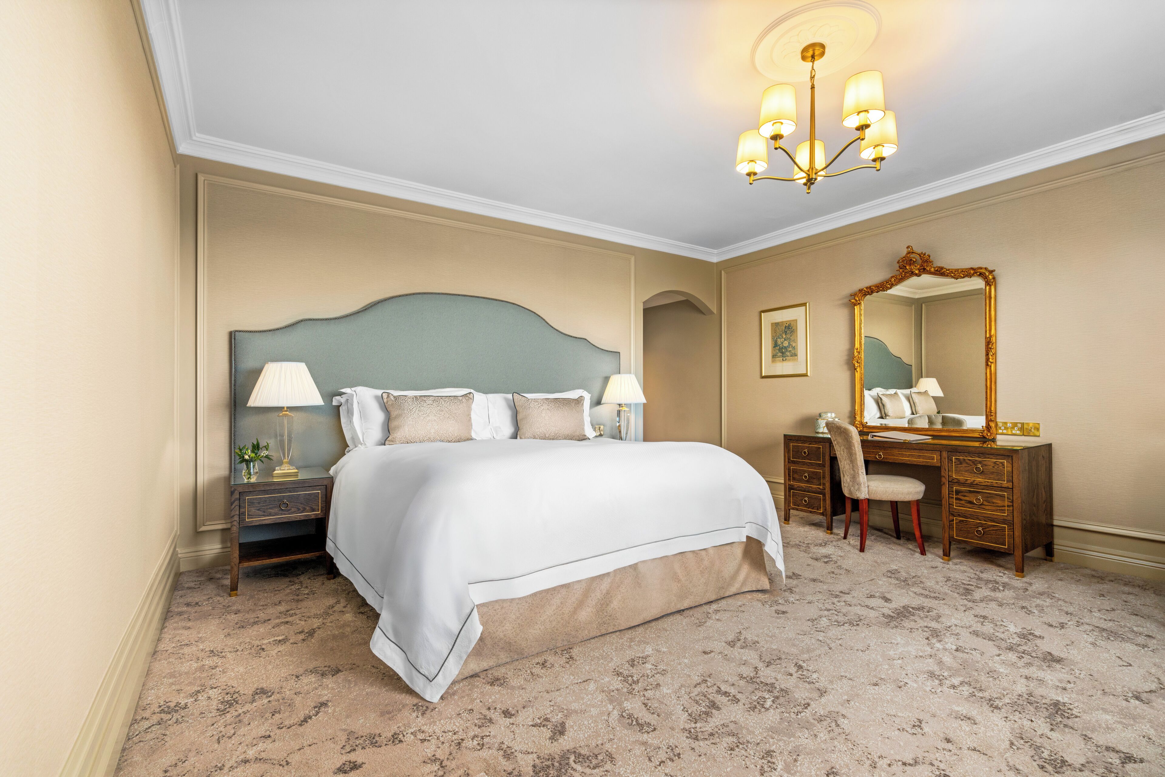Een slaapkamer met een groot bed, een bureau met stoel, een dressoir en een spiegel.