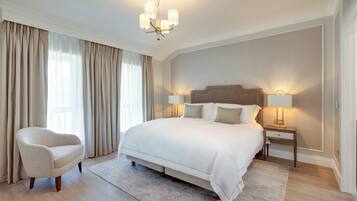 A spacious bedroom with a large bed, a nightstand with a lamp, a chair, and a chandelier.