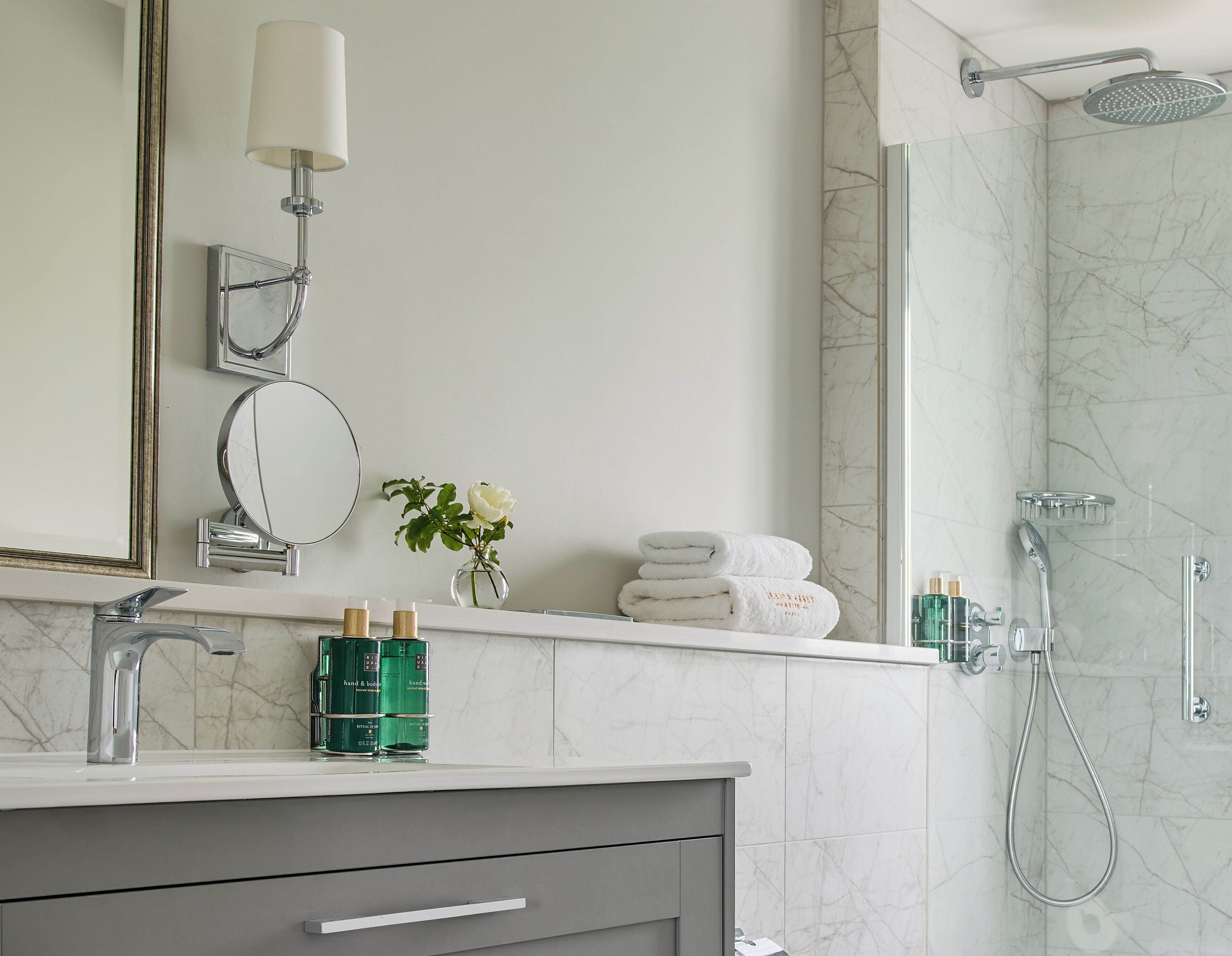 Un baño con pared de mármol, un espejo, toallero y ducha.