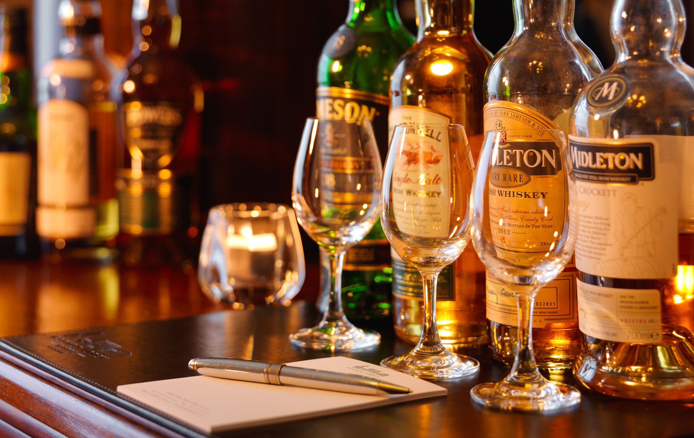 Un bar con varias botellas de whisky y vino, copas y un cuaderno sobre la barra.