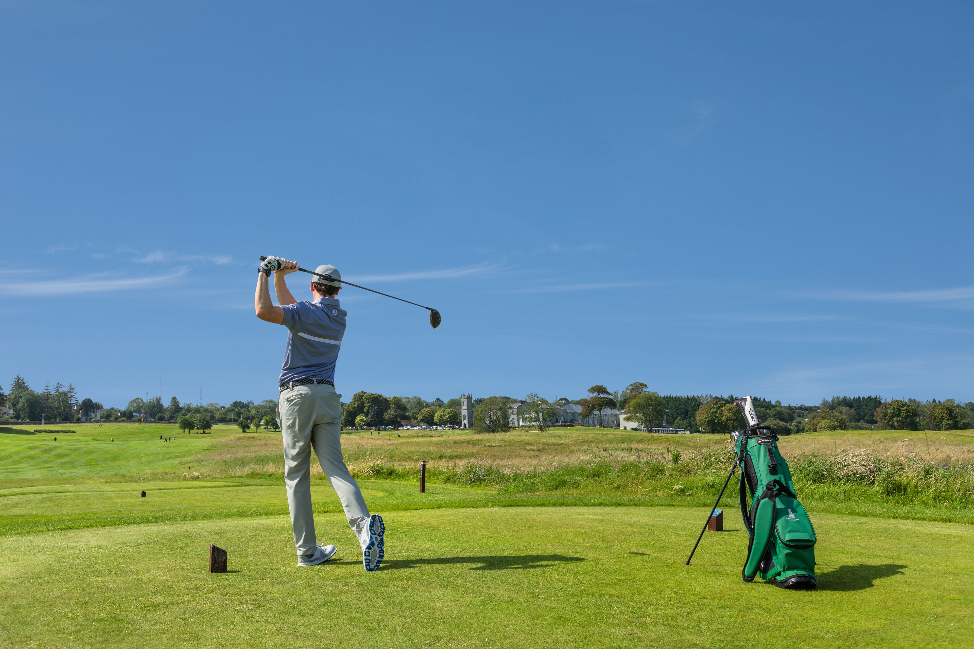 Henkilö pelaa golfia hyvin hoidetulla kentällä, ja lähellä on vihreä golfbägi.