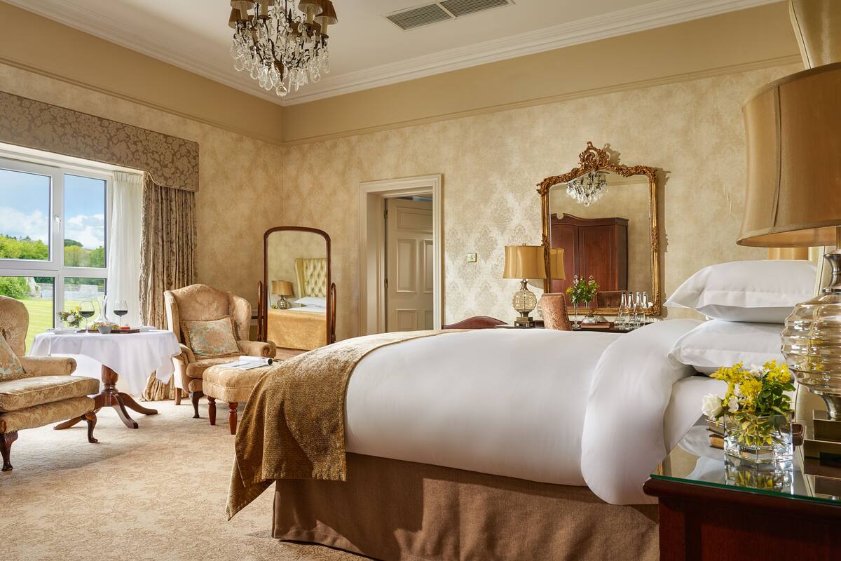 Ein geräumiges Hotelzimmer mit einem großen Bett, einer Sitzecke mit Stuhl und Tisch, einem großen Spiegel und Blick ins Freie.