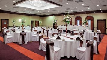 Uma sala de banquetes com mesas redondas, toalhas brancas e cadeiras com fitas marrons.