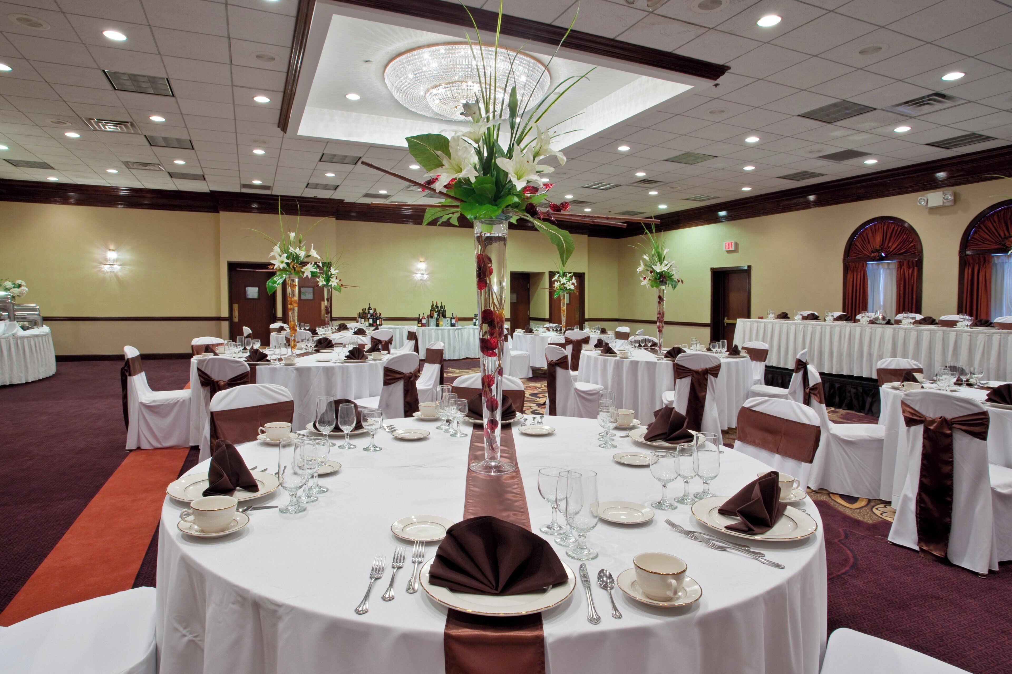 A banquet hall with round tables set for dining, featuring white tablecloths, silverware, and floral centerpieces.