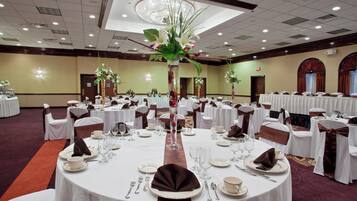 A banquet hall with round tables set for dining, featuring white tablecloths, silverware, and floral centerpieces.
