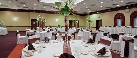 A banquet hall with round tables set for dining, featuring white tablecloths, silverware, and floral centerpieces.
