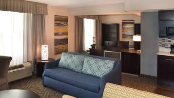 A hotel room with a sofa, a dining table, a small kitchen area, and a large window with curtains.
