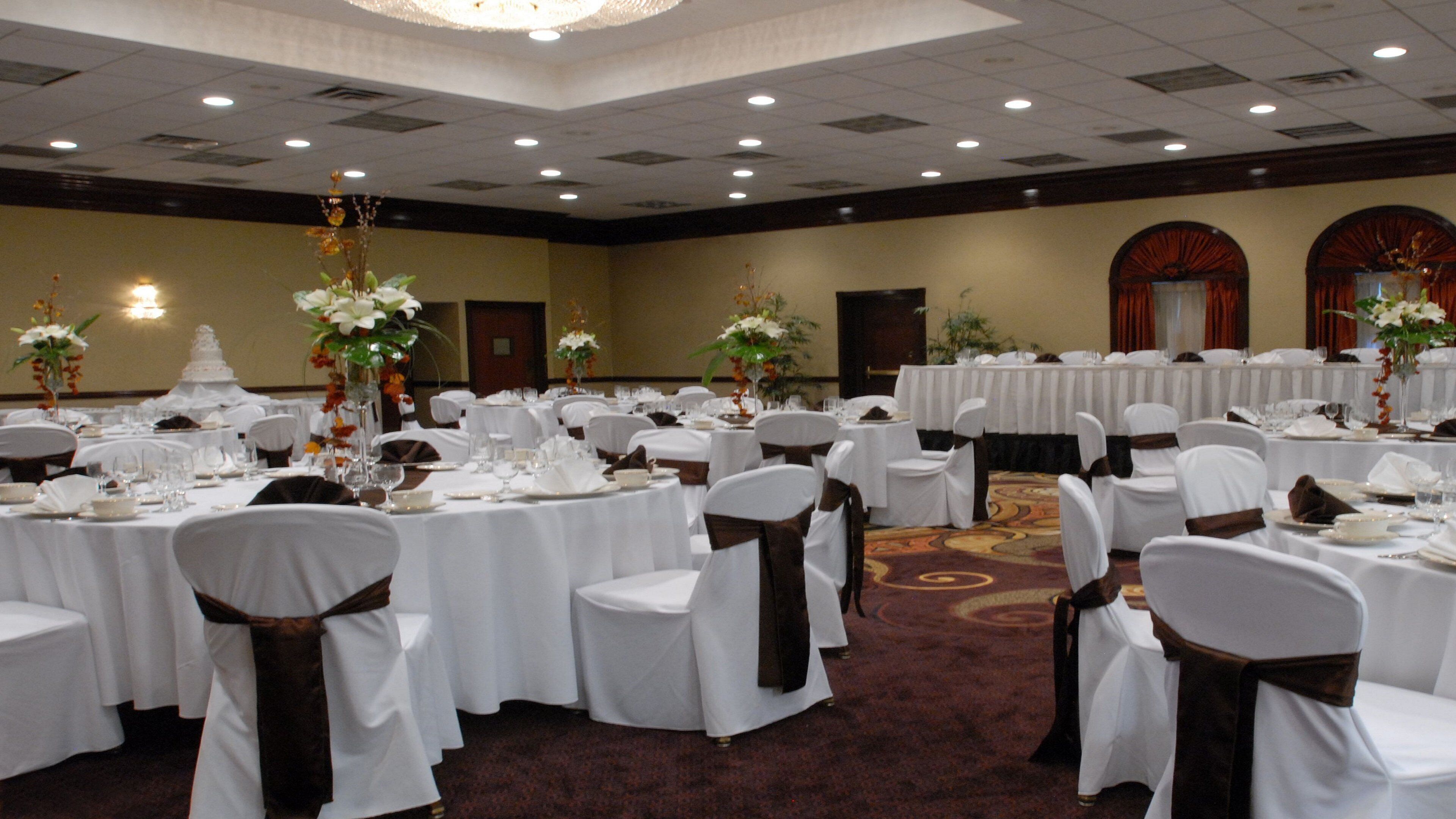 A banquet hall with round tables, white tablecloths, and chairs with brown sashes.