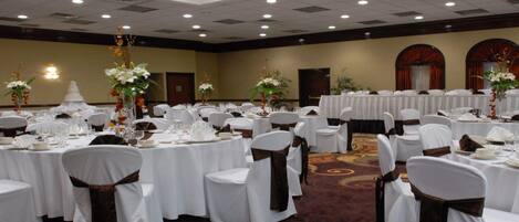 A banquet hall with round tables, white tablecloths, and chairs with brown sashes.