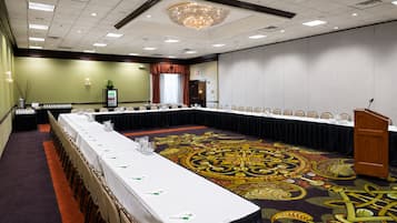 Une salle de conférence avec une longue table, des chaises, un pupitre et un tapis orné d’un motif géométrique.