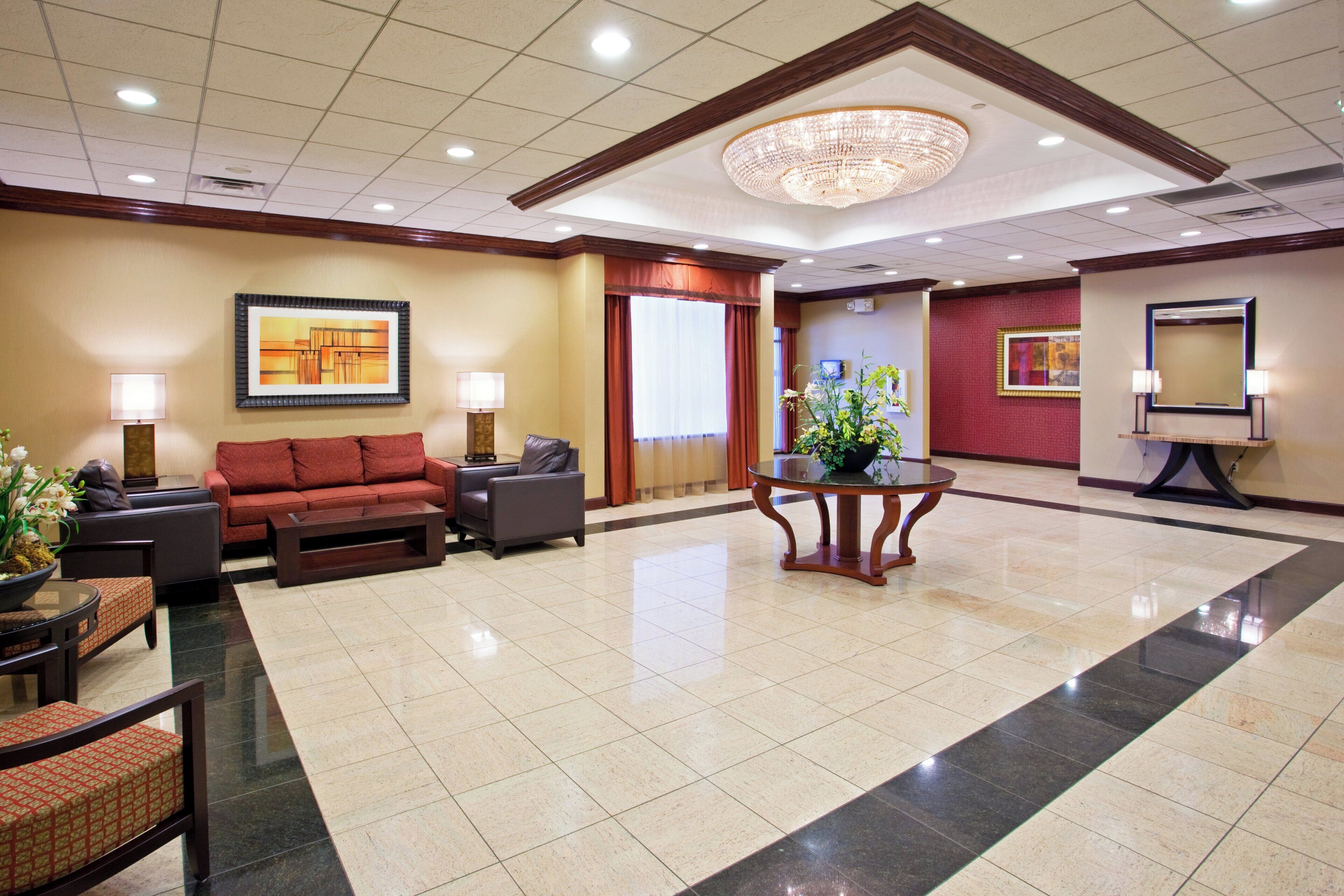 A lobby with a seating area, a chandelier, artwork on the walls, and a reception desk.
