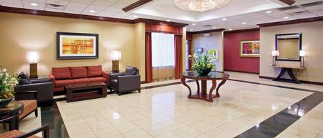 A lobby with a seating area, a chandelier, artwork on the walls, and a reception desk.