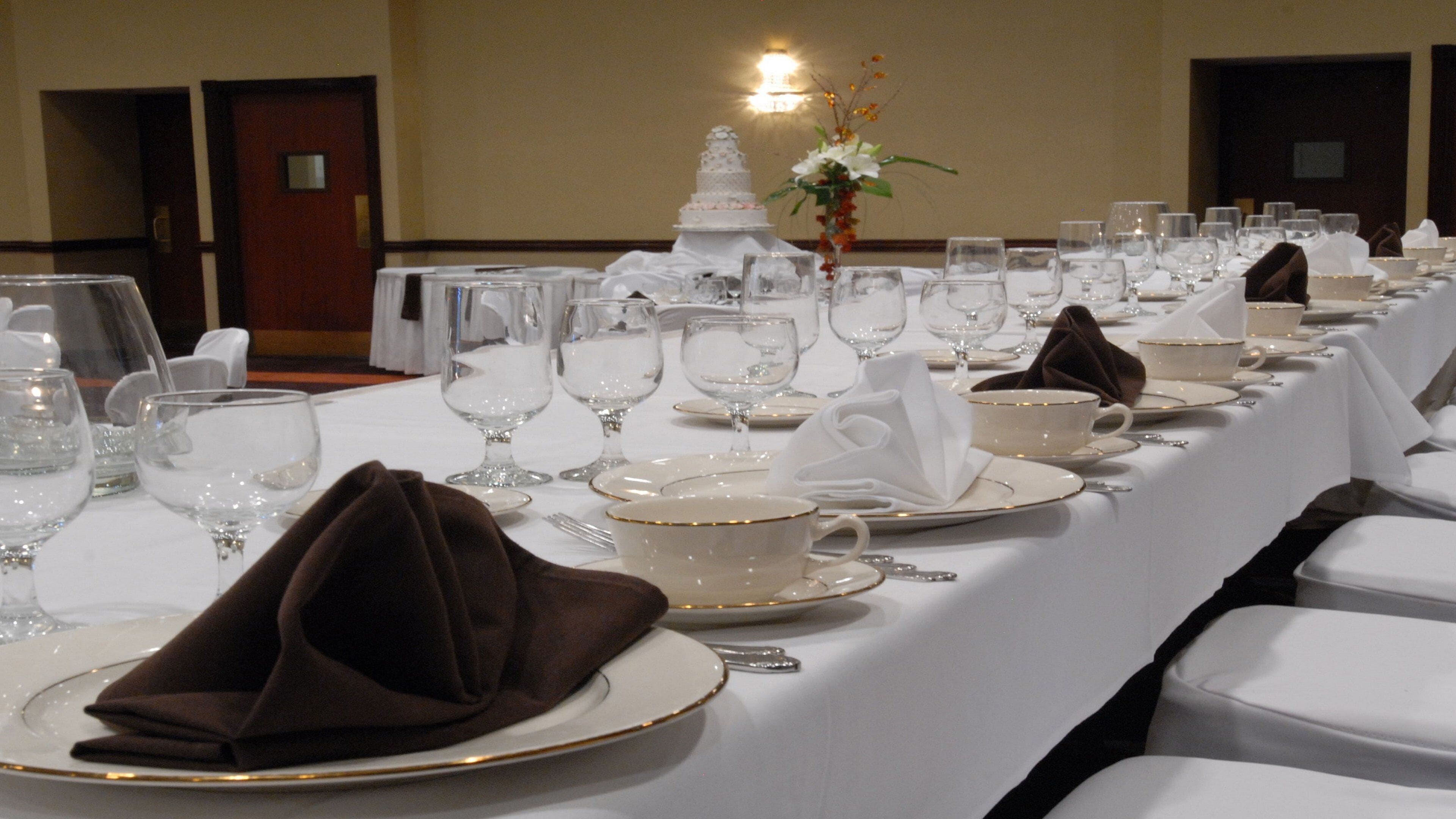 Une table de banquet dressée avec des nappes blanches, des assiettes, des verres et un centre de table.