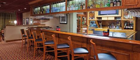 Una zona de bar con taburetes de madera, una barra con una caja registradora y estantes llenos de botellas.