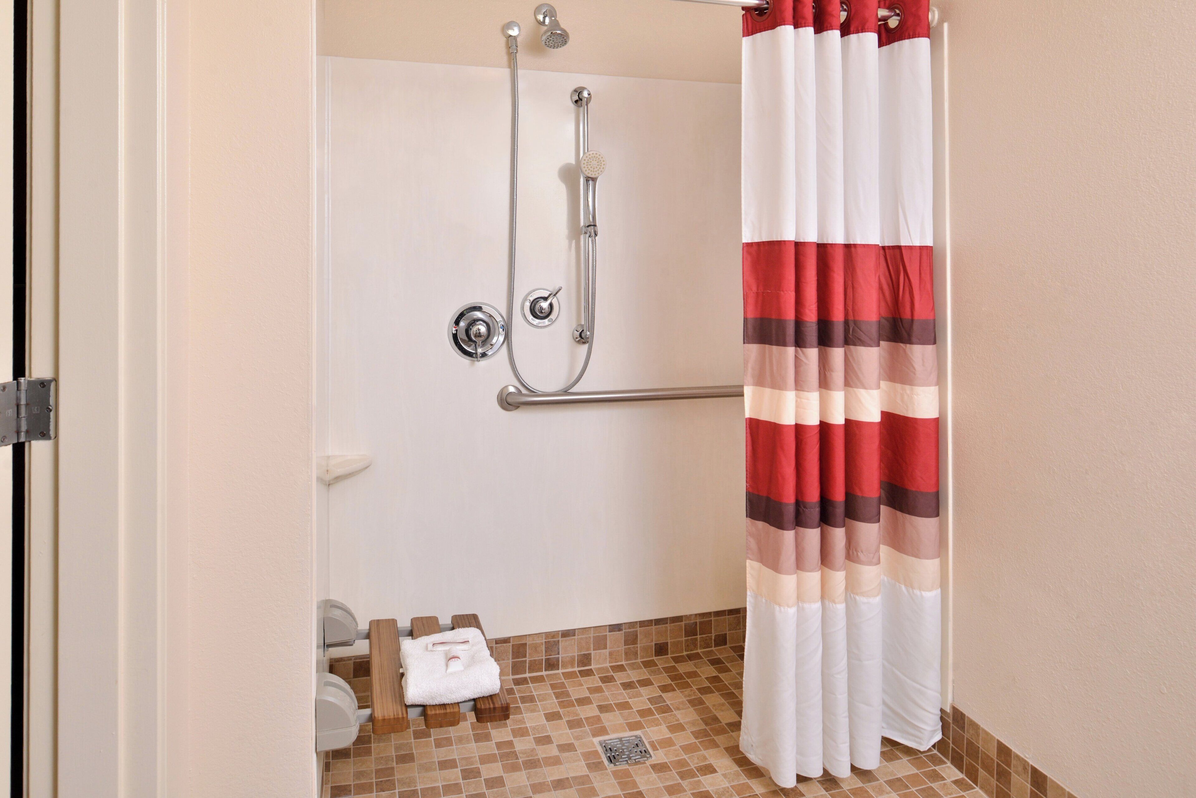 A shower with a handheld showerhead, a grab bar, and a towel rack with a folded towel.