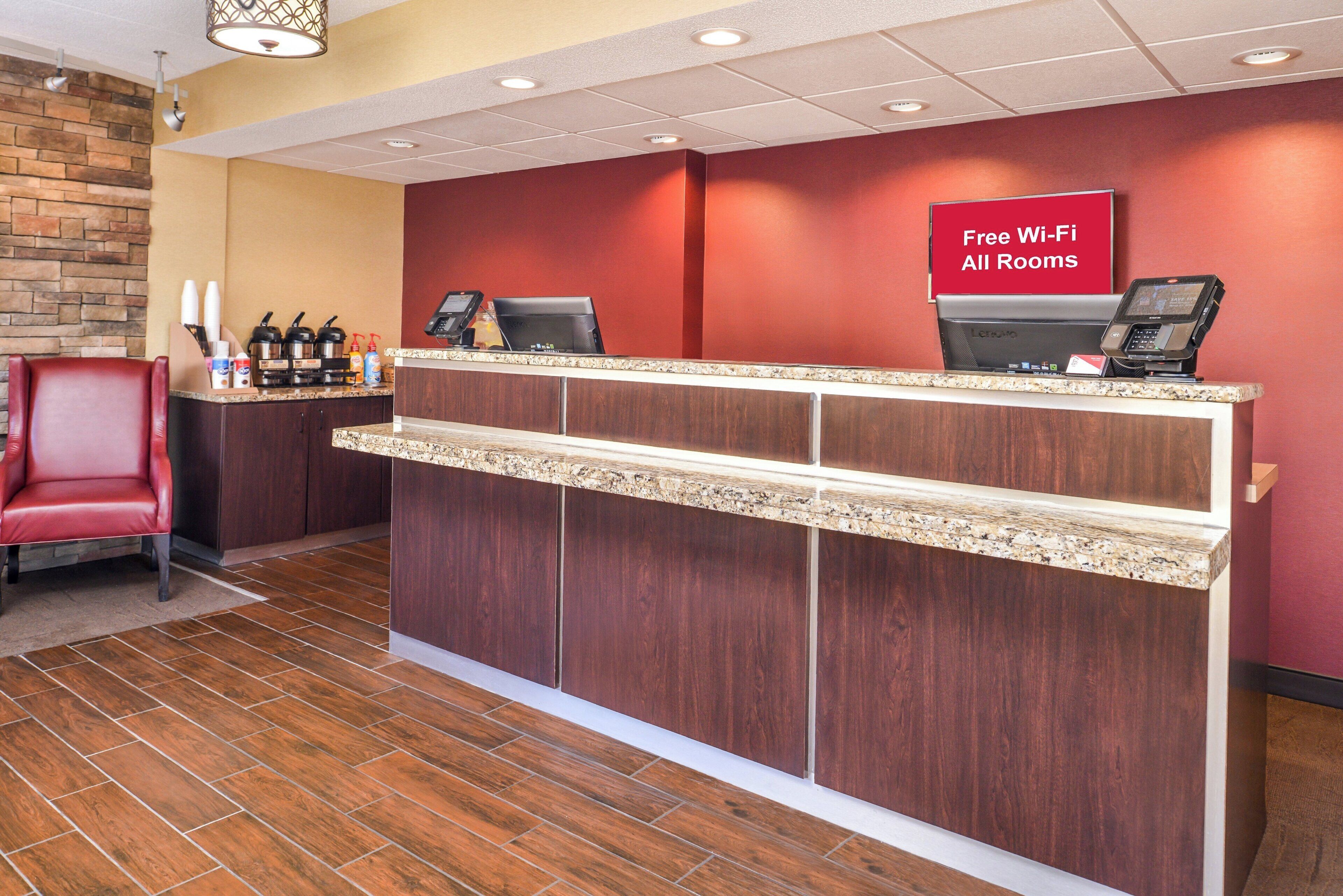 A reception desk with a digital kiosk, a red chair, and a sign indicating free Wi-Fi in all rooms.